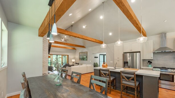 A modern kitchen with wooden beams, a dining area with a large table, and a central island with seating. - MORNING LIGHT (Swanton)