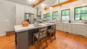 A modern kitchen with wooden beams, a large island with bar stools, and pendant lighting. - MORNING LIGHT (Swanton)