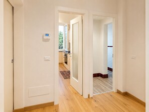 Ein Flur mit Holzboden, weißen Wänden und Blick in einen Küchenbereich mit Holzschränken und einem Fenster.
