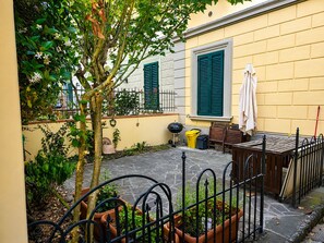A courtyard with a small tree, potted plants, a table with chairs, and a yellow building with green shutters. - Modern Terrace Retreat (Florence)
