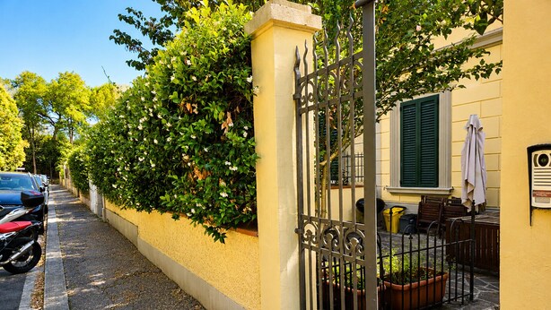 A yellow building with a metal gate, parked cars, and potted plants. - Modern Terrace Retreat (Florence)
