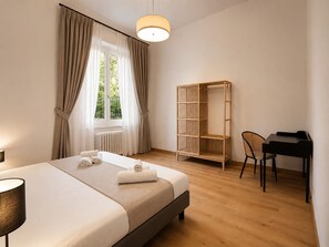 Ein Hotelzimmer mit Bett, Schreibtisch, Stuhl, Kleiderschrank und einem fenster mit Vorhängen.