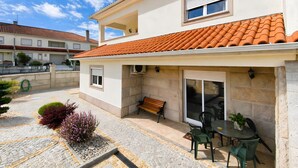 Ein zweistöckiges Gebäude mit einem Ziegeldach, einer Terrasse mit Tisch und Stühlen sowie einer Bank.