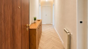 Un passadís amb una porta de fusta, un armari de fusta, una planta en test i un radiador.