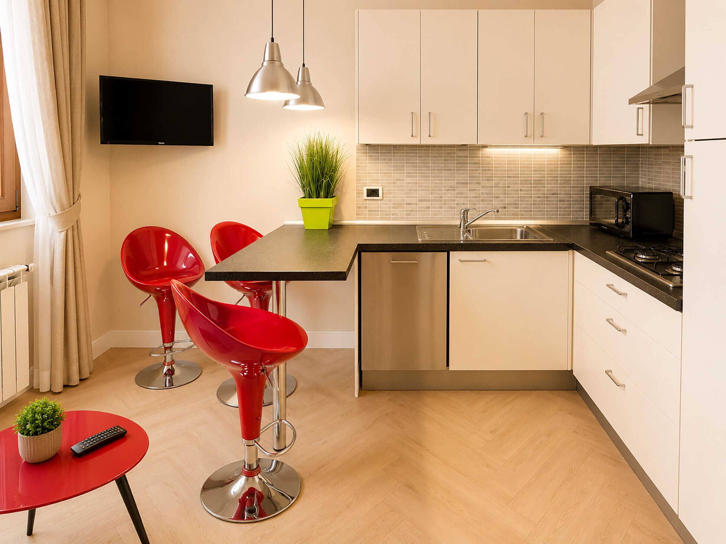 A modern kitchen with a dining area, including a TV, pendant lights, and red chairs.