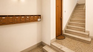 Un passadís amb una porta de fusta, uns caixets de correu, una escala i una petita finestra.