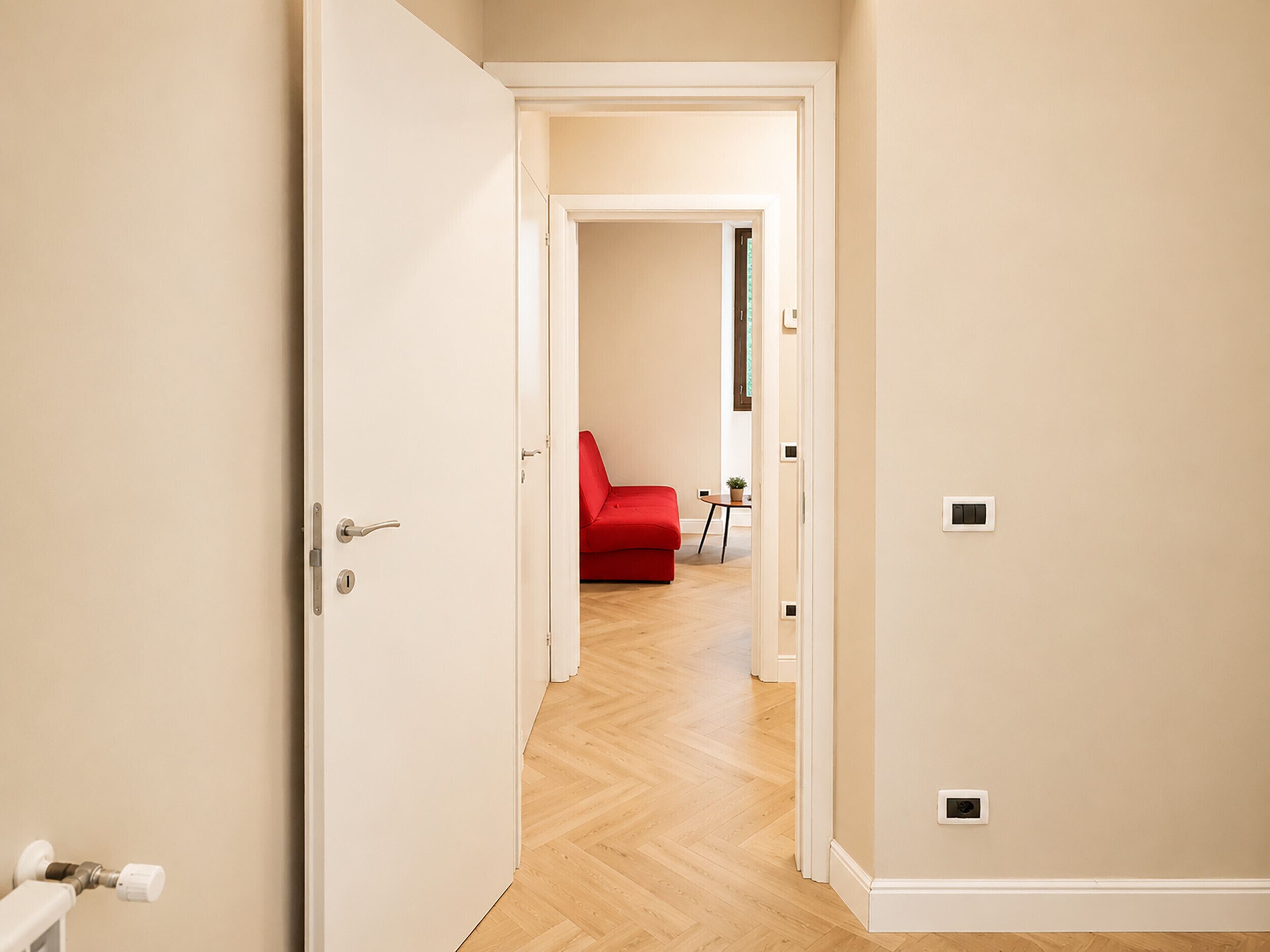 A hallway with a red sofa, a small table with a plant, and a door leading to another room.