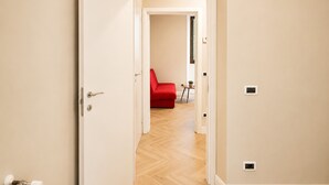 Un passadís amb un sofà vermell, una taula petita amb una planta i una porta que dóna a una altra habitació.