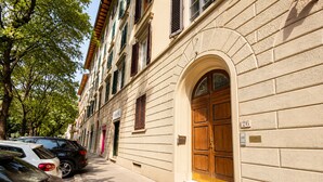 Un carrer amb cotxes estacionats i un edifici amb una gran porta de fusta i una finestra amb persianes.