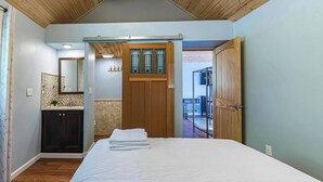 Une chambre à coucher avec un lit, une porte en bois, une salle de bain avec un miroir et une vue sur l’extérieur.
