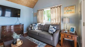Un salon avec un canapé, un téléviseur, une commode en bois et une fenêtre avec des rideaux.