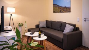 Uma sala de estar com um sofá, duas mesinhas, uma luminária, uma televisão e um quadro na parede.
