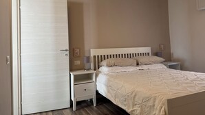 A bedroom with a bed, a nightstand, a drawer, a door, and a wall-mounted light.
