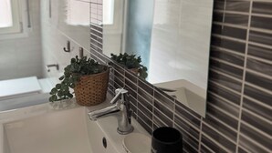 A bathroom with a white sink, a mirror, a potted plant, and a black mug.