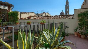 Un patio con plantas en macetas, una baranda de metal y un edificio con un campanario al fondo.