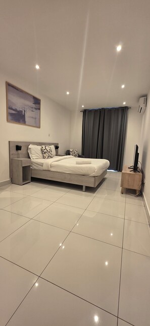 Une chambre à coucher moderne, avec un lit, des tables de chevet, un téléviseur à écran plat et un grand tableau abstrait accroché au mur.