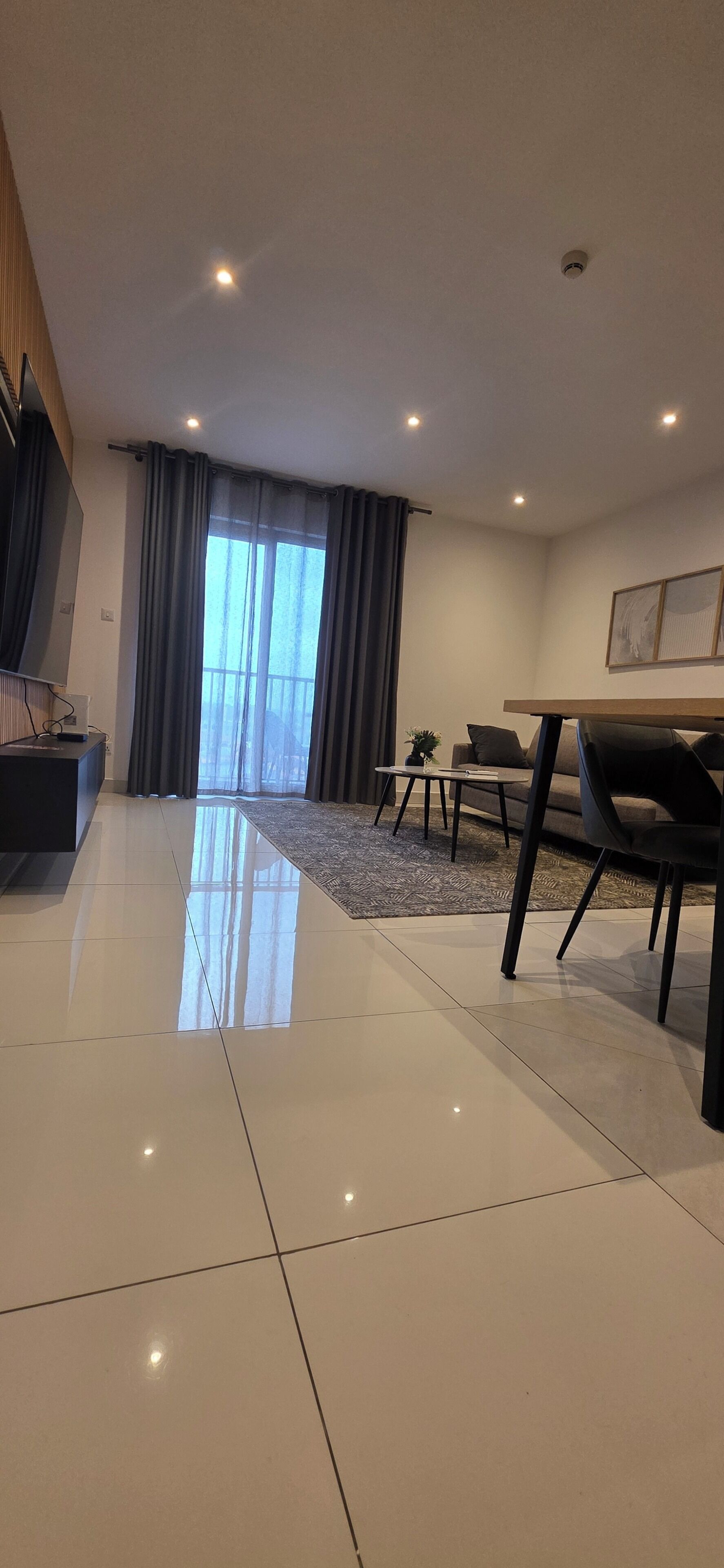 Una sala de estar moderna con un ventanal grande, una zona de comedor con mesa y sillas, y un televisor de pantalla plana montado en la pared.