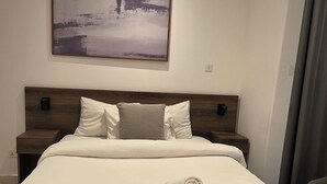 Habitación de hotel moderna con una cama grande, cabecera con detalles de madera, un cuadro colgado en la pared y una cama bien tendida con una toalla enrollada.