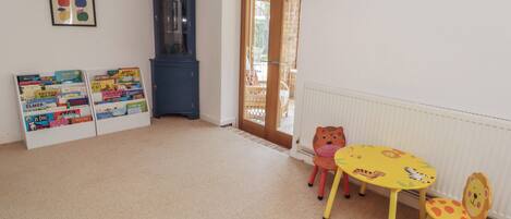 Una habitación con un armario de madera, una estantería llena de libros infantiles, una mesa redonda con sillas y un reloj de pared.