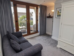 Una habitación con un sofá gris, un armario blanco y un ventanal corredero que da a un espacio exterior con muebles de mimbre y una botella de champán.
