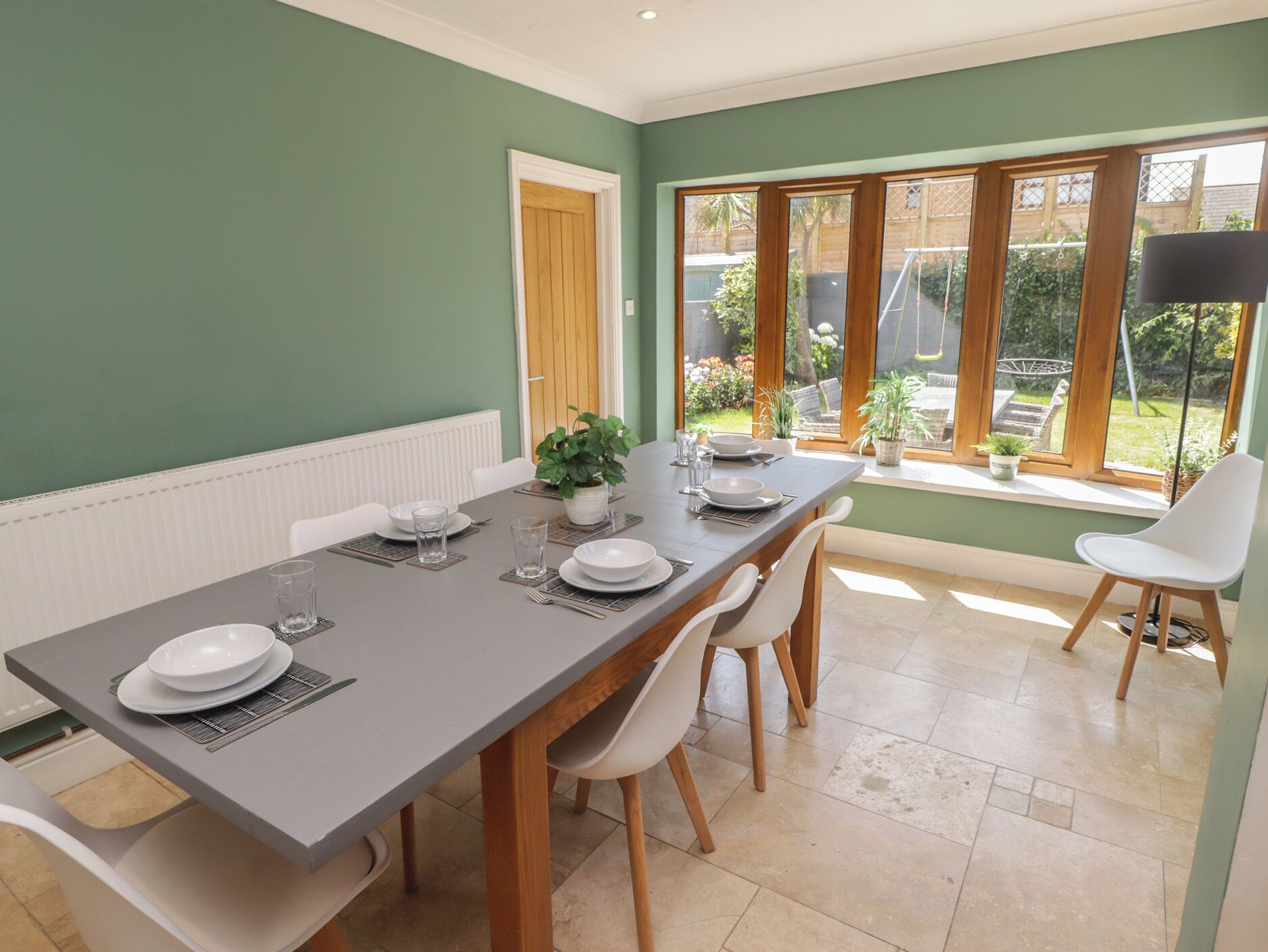 A dining area with a long table, chairs, and a view of the garden through large windows.