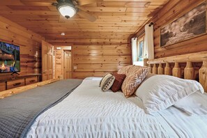 A wooden cabin bedroom with a bed, pillows, a television, and a ceiling fan. - Beautiful 5-bedroom lakefront cabin with AC in charming Necedah! (Necedah)