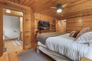 A wooden cabin bedroom with a bed, a television, and a ceiling fan.