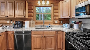 Une cuisine avec des meubles en bois, un lave-vaisselle en acier inoxydable, une cuisinière à gaz et une fenêtre donnant sur les arbres.