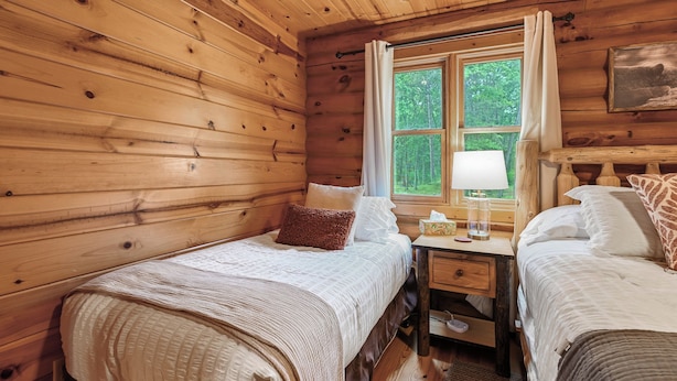 Une chambre de style cabine avec deux lits, une table de chevet, une fenêtre avec des rideaux et un tableau au mur.