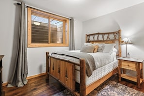 Een slaapkamer met een houten bed, een nachtkastje, een lamp en een raam met gordijnen.