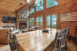 A rustic cabin interior with a dining table, chairs, a fireplace, and large windows. - Beautiful 5-bedroom lakefront cabin with AC in charming Necedah! (Necedah)