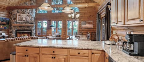A spacious kitchen with a large island, wooden cabinets, and a stone fireplace.