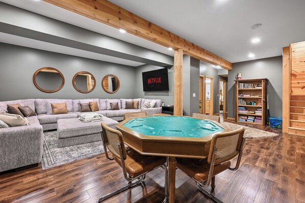 A living room with a sectional sofa, a pool table, and a bookshelf.