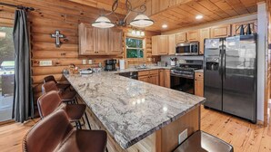 A log cabin kitchen with a granite countertop, stainless steel appliances, and wooden cabinets.