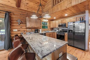 A log cabin kitchen with a granite countertop, stainless steel appliances, and wooden cabinets. - Beautiful 5-bedroom lakefront cabin with AC in charming Necedah! (Necedah)