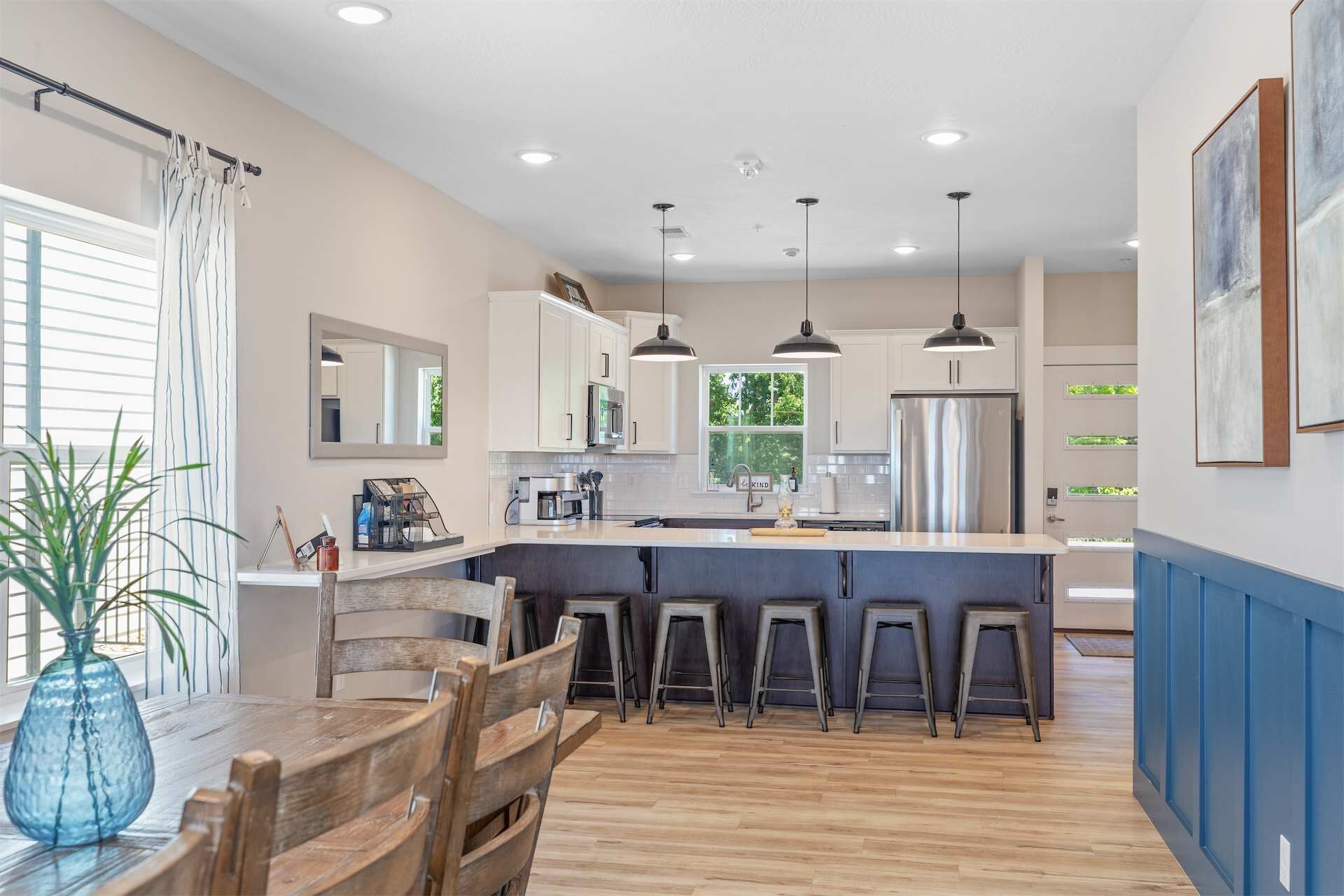 A modern kitchen with a central island, bar stools, and a dining table with chairs.