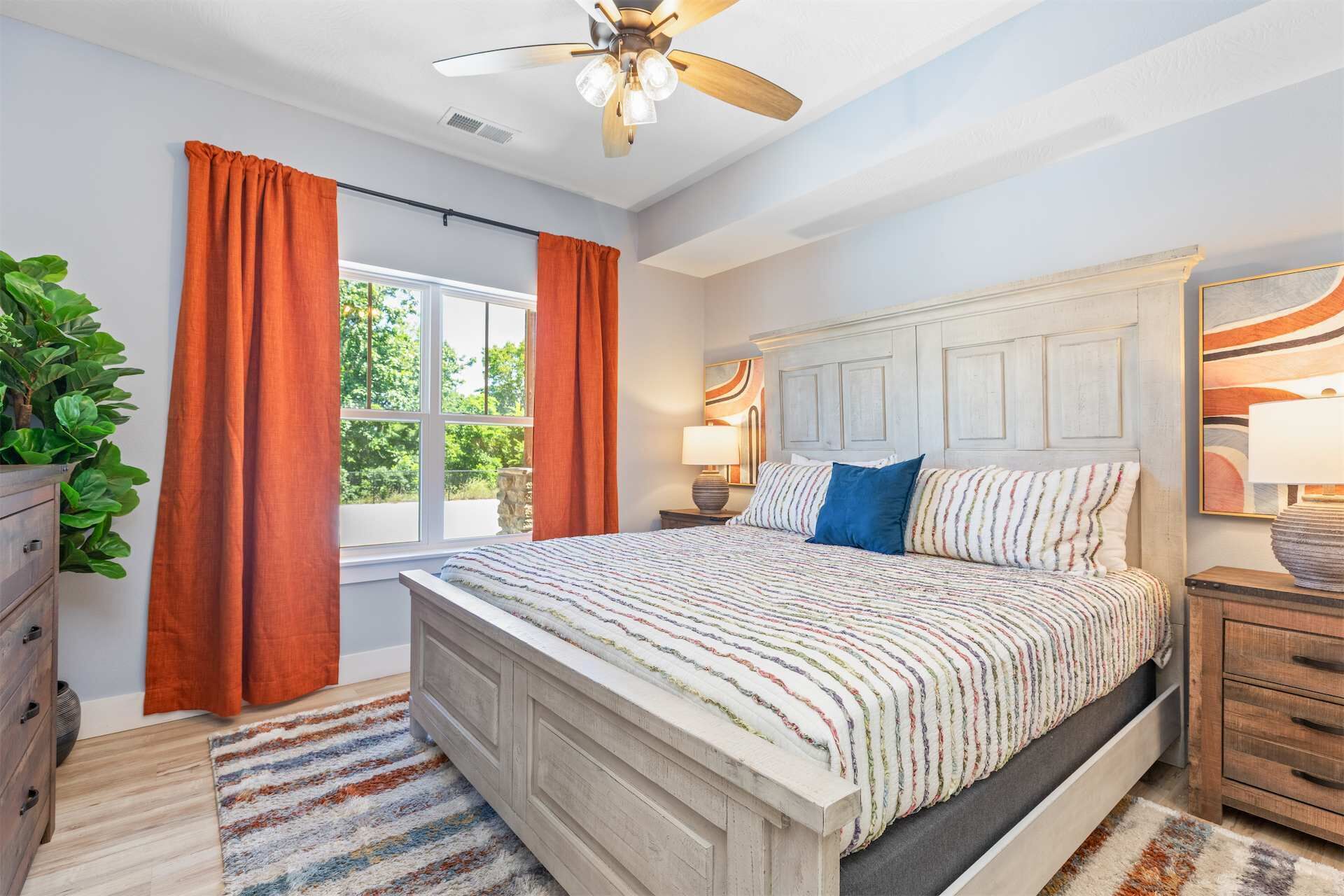 A bedroom with a bed, a ceiling fan, a window with curtains, a bedside lamp, and a nightstand.