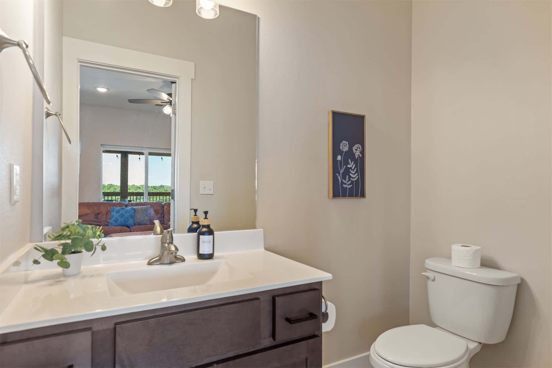 A bathroom with a white sink, dark cabinets, a toilet, and a framed floral artwork on the wall.