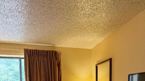 Une chambre d’hôtel équipée d’un bureau, d’une chaise, d’une télévision, d’une lampe, d’un climatiseur et d’une fenêtre avec des rideaux.