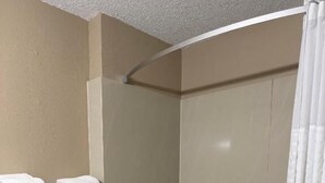 Une salle de bain avec une douche, une baignoire blanche, une chaise blanche et une étagère avec des serviettes.