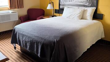 Habitación de hotel con cama, una silla, un escritorio, una lámpara y un cuadro grande en la pared.