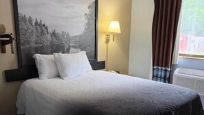 Une chambre d’hôtel avec un grand lit, une table de chevet, une lampe, une fenêtre avec des rideaux et un tableau accroché au mur.