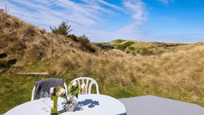 A table with a bottle and glasses, set against a backdrop of grassy hills and a clear sky. - 4 Star Holiday Home in Saltum (Saltum)