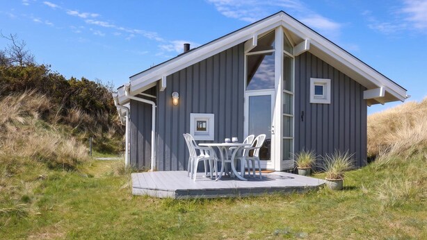A small, single-story cabin with a deck, a sliding glass door, and a white exterior. - 4 Star Holiday Home in Saltum (Saltum)