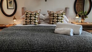 A neatly made bed with a grey blanket, two pillows with a leaf pattern, a mirror, and a wall-mounted elephant head decoration. - Bath House - Country Luxury on the Somerset Levels (Aller)
