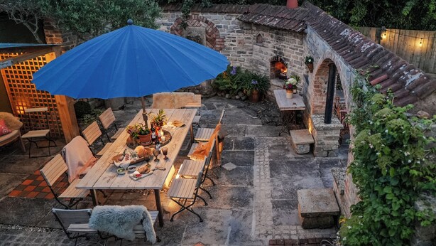 An outdoor patio with a stone wall, wooden furniture, and a blue umbrella. - Bath House - Country Luxury on the Somerset Levels (Aller)