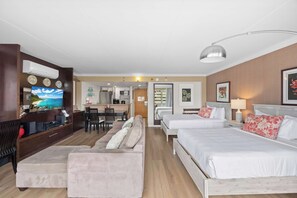 Une chambre d’hôtel équipée d’une télévision, d’un canapé, de deux lits, d’un coin repas et d’une cuisine à l’arrière-plan.
