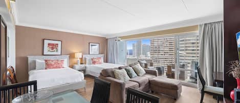 Habitación de hotel con cama, dos sofás, mesa de comedor, sillas y un ventanal con vista a la ciudad.