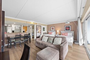A modern hotel room with a kitchenette, a sofa bed, a dining area, and a large window. - @ Marbella Lane - Iconic Waikiki City View Getaway (Honolulu)