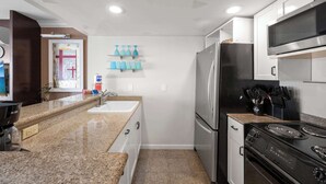 A compact kitchen with a granite countertop, stainless steel appliances, and a microwave above the stove. - @ Marbella Lane - Iconic Waikiki City View Getaway (Honolulu)